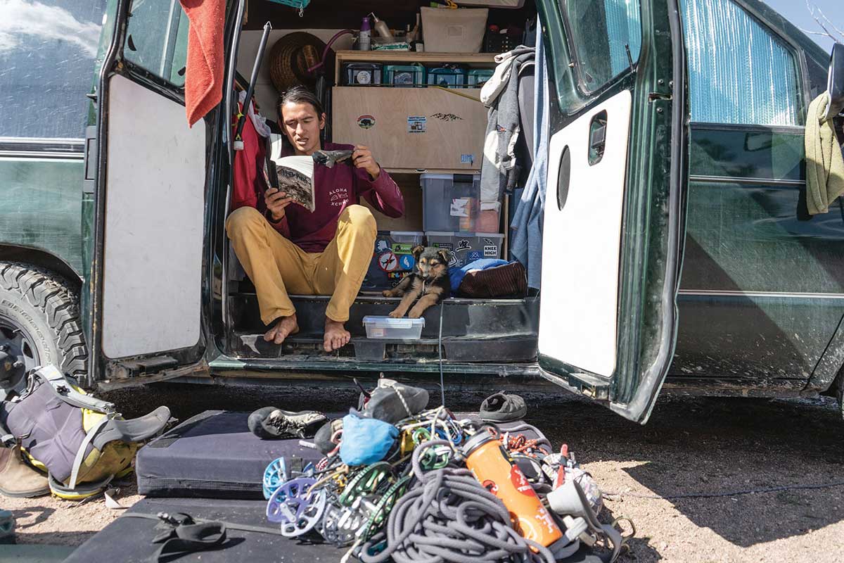 A climber reading a book in his van, next to a dog.